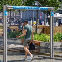 Mężczyzna przechodzący przez kurtynę wodną Katowickich Wodociągów S.A. w centrum Katowic podczas upalnego dnia — chłodząca mgiełka wodna na placu miejskim