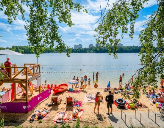 Plaża miejska nad jeziorem w Katowicach — wieża ratownicza MOSiR Katowice, plażowicze opalający się na piasku i kąpiący się w jeziorze, w tle zieleń lasów i osiedlowe wieżowce.